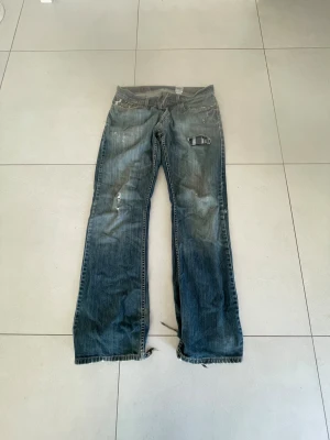 Levi's 517 - Säljer ett par klassiska Levi's 517 jeans i blå tvätt med slitna detaljer. Jeansen har slitningar vid fickor och benslut samt den ikoniska Levi's-lappen bak. 