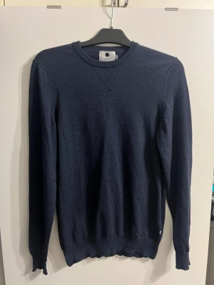 Mörkblå stickad tröja från NN07 - Snygg mörkblå stickad tröja från NN07 i modellen Barca, tillverkad i 100% extrafin ull. Tröjan har rund hals, ribbade muddar och lång ärm. Perfekt för dig som gillar stilrena och klassiska plagg med en modern touch.