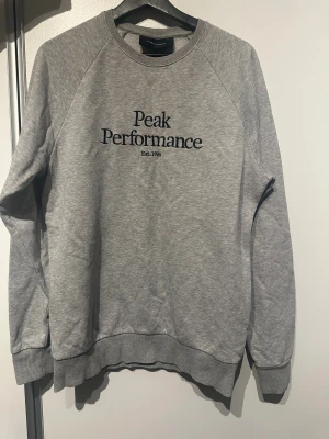 Grå Peak Performance sweatshirt  - Säljer en grå sweatshirt från Peak Performance i storlek M. Tröjan har rund hals, ribbade muddar och svart broderad logga på bröstet. 