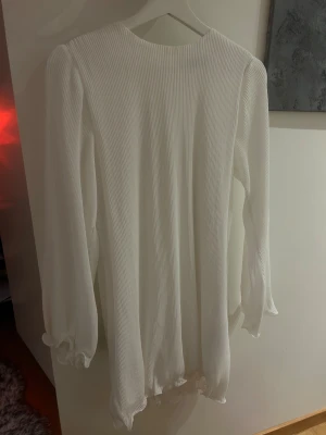 Vit ribbad kortklänning med volang - Supersöt vit kortklänning med ribbad struktur och långa ärmar. Klänningen har volangdetaljer vid ärmarna och i kjolslutet. (((((Klänningen är Oversize då jag inte skulle säga att klänningen uppfyller dess storlek)))))