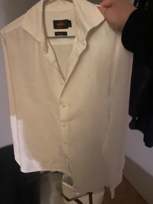 Vit linneskjorta Morris Slim Fit S - Fräsch vit skjorta från Morris i ren linne, modell Slim Fit. Klassisk krage, långärmad och med knappar framtill. Diskret broderad logga på bröstet. Perfekt för dig som gillar stilrena och luftiga plagg. Storlek S köptes på nk för 1500 och använt 2 ggr så inprencip i nytt skick 