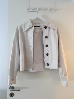 Beige jacka från Gina Tricot - Snygg beige jacka från Gina Tricot med stora bruna knappar och klassisk krage. 