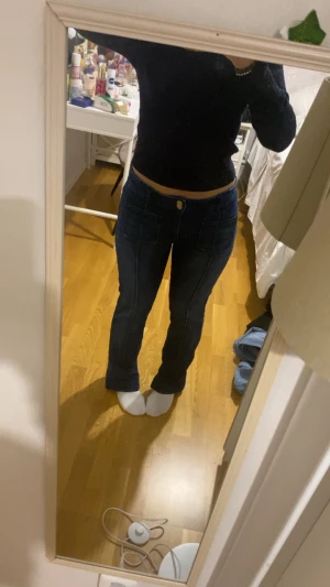 Blå bootcut jeans med låg midja - Snygga mörkblå jeans med bootcut och låg midja. Jeansen har framfickor med markerade sömmar och klassisk knappstängning. Passformen är loose och materialet är jeans. Perfekta för dig som gillar retrovibbar och vill ha en cool siluett.