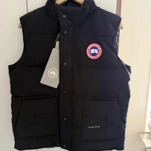 Canada Goose väst - Exklusiv väst från Canada Goose Red Label i klassiskt svart. En premiumväst med tidlös design och hög funktionalitet – perfekt balans mellan värme, komfort och stil. 