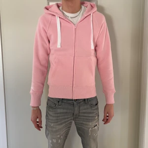 Ljusrosa hoodie från Russemarch M - Säljer en ljusrosa hoodie från Russemarch i storlek M. Helt ny! Nypris 749kr. Tröjan har dragkedja, huva med vita snören och två stora fickor framtill. Materialet är mjuk bomull och passformen är normal. Perfekt för chill dagar och snygg att matcha med jeans.