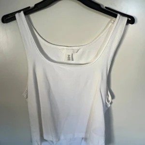 Vit linnetopp från H&M - En klassisk vit linnetopp från H&M i mjuk bomull. Toppen har breda axelband och rundad halsringning, perfekt för en enkel och clean look. Passar till allt och är superenkel att styla med andra plagg.