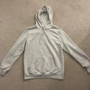 Ljusgrå hoodie Weekday - Säljer en stilren ljusgrå hoodie med huva och dragsnören. Tröjan har en klassisk känguruficka framtill och långa ärmar med muddar. Perfekt för dig som gillar en enkel och clean look. Passar till jeans eller joggers. Jag är 184 och 72 kg, tröjan är av märket ”weekday” och är i storlek S. Hör av dig om du har frågor eller vill diskutera pris!👍