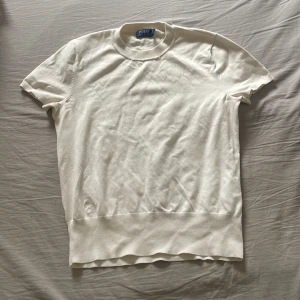 Vit kortärmad tröja från Polo Ralph Lauren - Vit kortärmad tröja från Polo Ralph Lauren i mjuk bomull. Klassisk rund halsringning och ribbad kant nertill. Enkel och stilren design som passar perfekt till jeans eller kjol. Snygg basic för garderoben. Se sista bilden för defekt men lättlagad för den som kan.Därav priset❤️