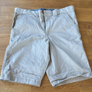 Beige shorts från Tommy Hilfiger - Snygga beige shorts från Tommy Hilfiger med klassisk design och raka ben. De har fickor fram och bak, bälteshällor och en diskret logga på bakfickan. Materialet är mjuk bomull som är skönt mot huden. Perfekt för varma dagar och chill stil. Storlek 18 är motsvarande mot XS ungefär skulle jag säga