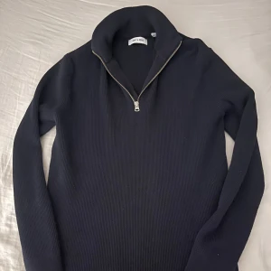 Svart stickad half zip-tröja Only & Sons - Svart stickad tröja från Only & Sons med half zip-dragkedja och hög krage. Tröjan är ribbad och har lång ärm, perfekt för kyligare dagar. Enkel och stilren design som funkar till många outfits.