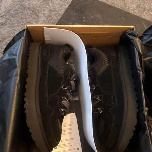 UGG LOWMEL  - Säljer ett par svarta sneakers från UGG. Storlek 43. Oanvända köpte i NK. finns i Stockholm eller fraktas. 