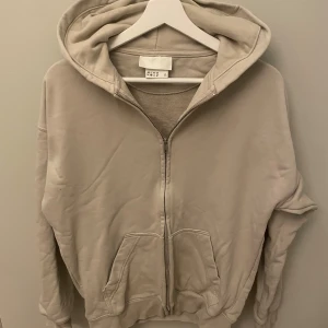 Beige hoodie med dragkedja från H&M - Säljer en beige hoodie från H&M i storlek XS. Tröjan har dragkedja framtill, huva och två stora fickor. Tillverkad i mjuk bomullsmix och har en avslappnad passform med långa ärmar. Perfekt för chill dagar eller när du vill vara extra bekväm.