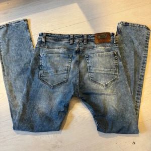Blå Diesel jeans slim fit - Säljer ett par klassiska blå jeans från Diesel med snyggt slitna detaljer och slim fit. Jeansen har fem fickor, normal midja och tydliga Diesel-loggor på bakficka och knapp. Perfekta för dig som gillar en tidlös och avslappnad look. 33-34 sitter som 31-32