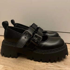 Buffalo svarta chunky ballerinaskor - Buffalo ballerinaskor i svart skinn med grov plattformssula och dubbla spännen över foten. Rund tå och robust design som ger en edgy vibe. Perfekt för dig som gillar statement-skor med extra höjd och coola detaljer. Kommer med lådan och använt dom 3 gånger säljer dom för att det är inte min still 