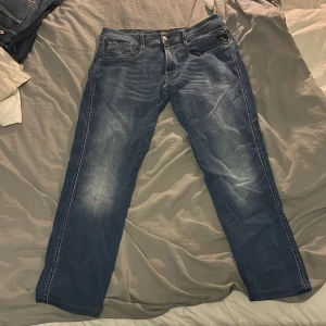 Replay Anbass jeans blå, stl 31 - Säljer ett par snygga Replay Anbass jeans i klassisk blå tvätt med slitningar. Jeansen har fem fickor, raka ben och normal passform. Perfekta för dig som gillar stilrena och bekväma jeans med lite edge. För endast 349kr!
