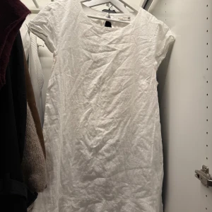 Vit linneklänning med kort ärm - Enkel och stilren vit klänning från Indiska i linne med korta ärmar och rund halsringning. Perfekt för varma dagar med sin luftiga känsla och raka passform. Snygg att styla med sandaler eller sneakers. Från Nelly