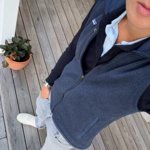 Mörkblå fleeceväst från Patagonia - Säljer en mörkblå fleeceväst från Patagonia med dragkedja framtill och två sidofickor. Västen har en enkel, clean look och är perfekt att slänga på över en skjorta eller tröja. Bra omhändertagen, skick 8/10. 