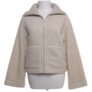 Beige teddyjacka med dragkedja - Mysig beige teddyjacka med dragkedja framtill och två stora fickor. Jackan har en hög krage och är tillverkad i fluffigt teddy-material som ger en chill och trendig look. Perfekt för lager-på-lager och att hålla sig varm under kyliga dagar.