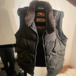 Mörk grön limiterad dunväst från Parajumpers  - Mörk grön limiterad dunväst med fluffig brun krage från Parajumpers. Västen har dragkedja framtill, två snedställda fickor med knappar och dragkedjor samt orange detalj på sidan. Använd två gånger, perfekt för en eligant höst stil. 