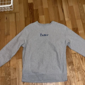 Grå sweatshirt från Butter, medium - Säljer en stilren grå sweatshirt från Butter i storlek medium. Tröjan har rund halsringning, lång ärm och blå Butter-logga broderad på bröstet. Mjuk insida i fleece som gör den extra skön att ha på sig. Perfekt för en chill och avslappnad look.