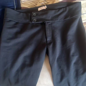 Svarta bootcut-byxor från Nelly - Snygga svarta bootcut-byxor från Nelly i storlek S. Byxorna har hög midja, två knappar framtill och är tillverkade i ett mjukt, stretchigt material som sitter skönt. Perfekt för dig som gillar en klassisk och stilren look. Nypris 350