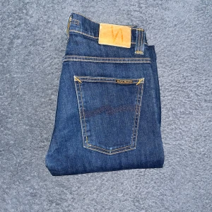 Nudie Jeans Average Joe blå  - Säljer ett par klassiska blå Nudie Jeans Average Joe i rak modell. Jeansen har snygga kontrastsömmar, Midja 36cm, längd 98cm. OBS jeansen är uppsydda för att motsvara L30 men utgå ifrån måtten !  Ifall det inte finns någon bild i annonsen där jag bär plaggen jag säljer så är det för att jag ej kan ha storleken heller passformen, så kolla måtten för storlek och googla på modellnamnet för passform 😉2