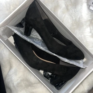 Svarta mockapumps från Tamaris - Snygga svarta pumps från Tamaris i mjuk mocka med rund tå och låg klack. Klassisk och stilren design som passar perfekt till både jeans och klänning. Skorna har en bekväm passform och är lätta att matcha med olika outfits. Storlek 38 och använd en gång. Nypris 599kr