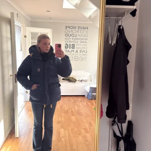 Mörkblå dunjacka från Fjällräven - Säljer en mörkblå dunjacka från Fjällräven med huva och gula snören. Jackan har två stora fickor framtill, även fickor under dem fickorna man ser, den har två stora fickor inne i jackan och en liten ficka inne i jackan. Så totalt har jackan 7 fickor, dragkedja och knappar. Klassisk badge på bröstet och riktigt fluffig passform som håller dig varm hela vintern. Jag säljer den för ett bra med tanke på att den typ är ny. Har använt den 3 gånger. Säljer den för att det inte var min stil på jacka. 