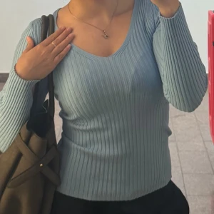 Ljusblå ribbad långärmad tröja - Säljer en ljusblå ribbad tröja med v-ringning och långa ärmar. Tröjan är figurnära och har en snygg, enkel design som passar perfekt till jeans eller kjol. Supermjuk och stretchig, perfekt för lager på lager under höst och vår.