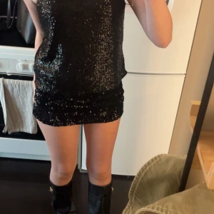 Svart glittrig paljettopp H&M - Svart topp från H&M med tunna axelband och glittriga paljetter över hela. Toppen har en rak passform och är ärmlös, perfekt för att sticka ut med sin glittriga look. Materialet är polyester och toppen har en snygg v-ringad detalj framtill.