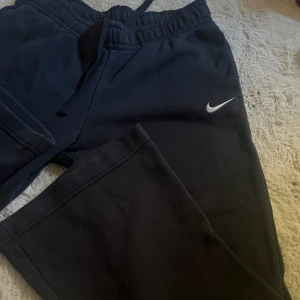 Mjukisbyxor från Nike  - Svarta mjukisbyxor från Nike med klassisk vit swoosh-logga på ena benet. Byxorna har en bootycut passform och är perfekta för chill eller träning. 