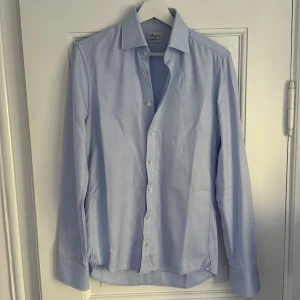 Slim fit blå skjorta från Stenströms - Snygg ljusblå skjorta från Stenströms i slim fit-modell. Skjortan är tillverkad i bomull och har diskret struktur, klassisk krage och vita knappar. Ärmsluten har ett mönstrat tyg på insidan för en extra detalj. Ass snygg som kommer få dig alla guzzar nypris på hela 1600kr men mitt pris endast 220 kr köp din nya stenströms skjorta! Vid frågor skriv bara!