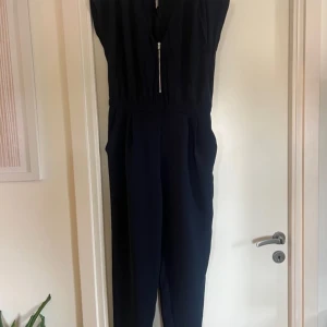 Mango Suit byxdress, storlek M - Snygg jumpsuit, mörkblå med v-ringning och dragkedja framtill. Den har korta ärmar och fickor i sidorna.