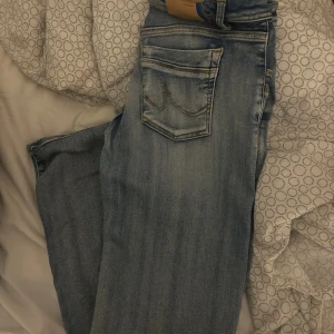 Molly bootcut jeans låg midja 29/34 - Snygga ljusblå bootcut jeans från t.b Studio Design, modell Molly. Jeansen har låg midja, klassisk femficksdesign och slitna detaljer för en cool look. Perfekta för dig som gillar retrovibbar och vill ha ett par jeans med lite extra attityd.