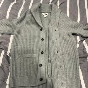 Grå ribbstickad kofta från M&S - Säljer en grå ribbstickad kofta från M&S i storlek S. Koftan är tillverkad i ull och materialet känns riktigt skönt på säljes då den är för liten för mig och ej kommer till användning riktigt fint skick:)