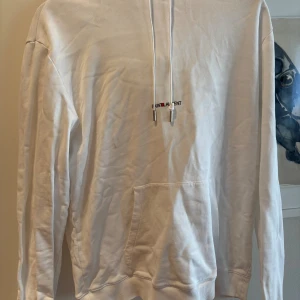  Saint Laurent hoodie - Vit hoodie från Saint Laurent med broderad logga på bröstet. Klassisk känguruficka framtill, dragsko i huvan och ribbade muddar. Tillverkad i mjuk bomull, perfekt för en clean och stilren look. Finns några fläckar/de flaws (se bilderna) 