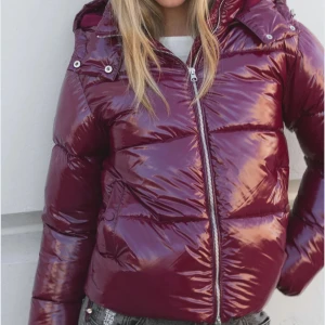 Vinröd pufferjacka med huva - Säljer en glansig vinröd pufferjacka från Nelly med huva och dragkedja framtill. Jackan har en quiltad look och är perfekt för kalla dagar. Den har långa ärmar och en schysst oversized passform som ger en cool vibe. Passar dig som gillar att sticka ut med färg. Helt oanvänd. 