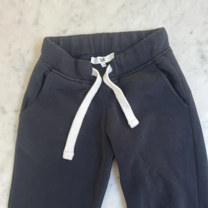 Svarta mjukisbyxor med snörning XXS - Svarta mjukisbyxor från R i storlek XXS. Byxorna har bred resår i midjan och vit snörning framtill. Mjukt bomullsmaterial och två sidofickor. Perfekta för chill dagar eller när du vill vara bekväm.