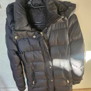 Svart dunjacka Rockandblue stl 34 - Snygg svart dunjacka från Rockandblue med guldig dragkedja och detaljer. Jackan har hög krage, två fickor med dragkedja och Rockandblue-logga på ärmen. Perfekt för kalla dagar och riktigt skön att bära. Pris går att diskutera