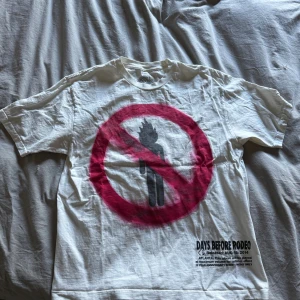 Travis Scott vit t-shirt L - Vit t-shirt från Days Before Rodeo med stor grafisk print framtill i rött och svart och textdetaljer både fram och bak. Skön passform och klassisk rund hals. Perfekt för dig som gillar streetwear och Travis Scott-vibbar. OBS finns en liten fläck på insidan på T-shirten, syns på bilden med tagen.