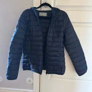 Mörkblå pufferjacka från Blue Motion - Säljer en mörkblå pufferjacka från Blue Motion i storlek S. Jackan har huva, dragkedja framtill och två sidofickor.