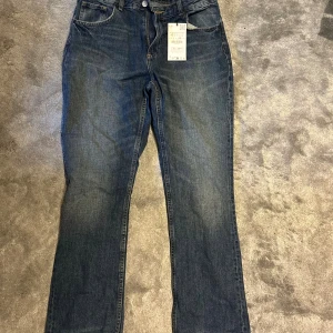 Zara Bootcut jeans blå strl 42 - Snygga blå bootcut jeans från Zara i storlek 42. Klassisk femficksmodell med normal passform och lätt utsvängda ben. Jeansen är tillverkade i bomull och har en mörkblå tvätt med subtila slitningar. Perfekta för dig som gillar en tidlös look.
