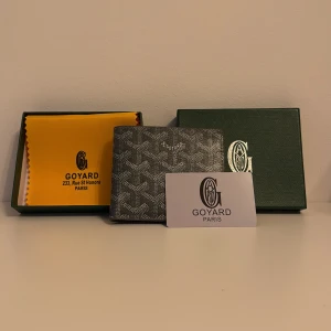 Svart mönstrad plånbok från G yard - Exklusiv svart plånbok från G yard med ikoniskt grafiskt mönster och diskret logga framtill. Plånboken är tillverkad i skinn och har flera kortfack på insidan. Kommer med original ask och tygpåse, perfekt för dig som gillar lyxiga accessoarer.