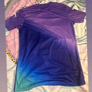 AC Milan x Puma lila-blå fotbollströja - Snygg AC Milan fotbollströja från Puma i en cool gradient från lila upptill till blå och turkos nedtill. Tröjan har korta ärmar, rund halsringning och tryck med Emirates Fly Better på bröstet. Tillverkad i lätt och ventilerande funktionsmaterial.