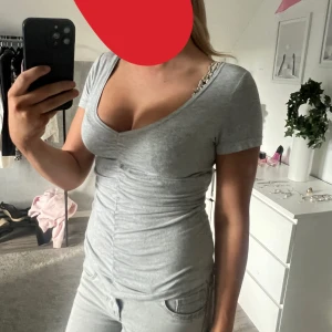 Grå v-ringad topp med rynk - Säljer en ljusgrå topp med v-ringning och korta ärmar. Toppen har snygg rynkdetalj framtill som ger en smickrande passform. Tillverkad i mjuk bomull och passar perfekt till jeans eller kjol.