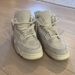 Nike Air Jordan 4 i beige canvas - Säljer ett par Nike Air Jordan 4 sneakers i beige canvas med klassisk siluett och snörning. Skorna har vita detaljer, rund tå och platt sula. Diskret Jumpman-logga på plösen och hälen. Perfekta för dig som gillar stilrena och unika sneakers.