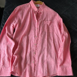 Rosa linneskjorta från Lindbergh - Snygg rosa skjorta från Lindbergh i relaxed fit, tillverkad i en skön mix av bomull och linne. Skjortan har klassisk krage med knappar, bröstficka och långa ärmar. Perfekt för dig som gillar en avslappnad men stilren look.