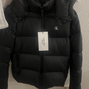 Svart pufferjacka Calvin Klein Jeans S - Svart pufferjacka från Calvin Klein Jeans i st S. Yttermaterialet är återvunnen nylon och fodret är återvunnen polyester med dunfyllning. Helt ny oanvänd med lappen på