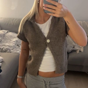 zara stickad tröja - Säljer en brun stickad kofta med korta ärmar och en stor vit knapp framtill. Koftan har en croppad passform och ribbade kanter vid ärmslut och nederkant. Perfekt att slänga över en t-shirt för en chill look.