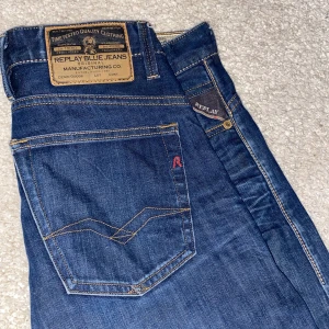 Replay Blue Jeans Herr slim fit - Snygga blå jeans från Replay med klassisk femficksdesign och raka ben/slim fit. Jeansen har tydliga kontrastsömmar, läderpatch bak och Replay-logga, och diskreta slitningar. Waist= 31 length = 32